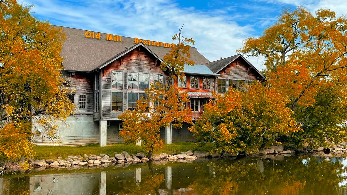 exterior of Old Mill Restaurant with body of water in foreground surrounded by trees during fall in Tennessee, USA